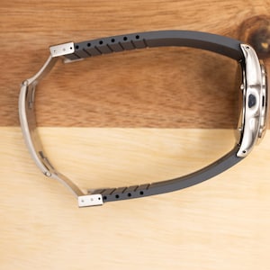 May include: A silver wristwatch with a black rubber strap. The watch is on a wooden surface.