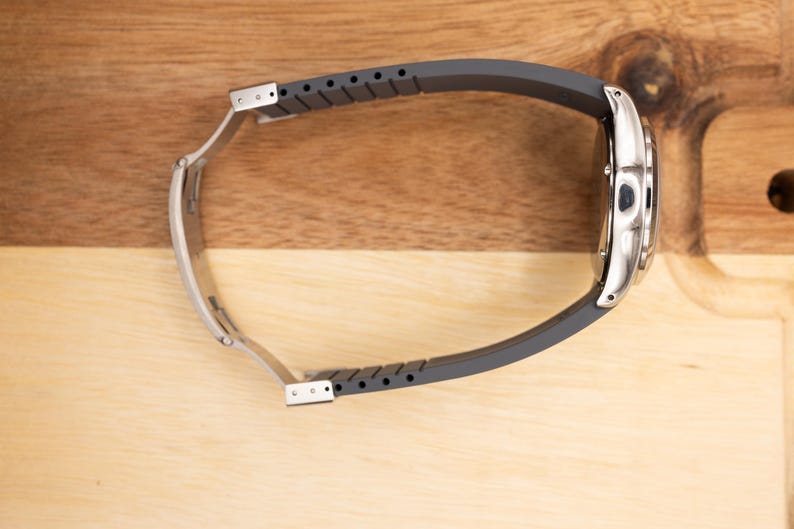 May include: A silver wristwatch with a black rubber strap. The watch is on a wooden surface.