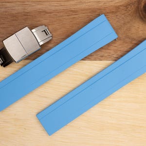 May include: Two light blue watch straps with a silver watch buckle. The straps are made of a rubber-like material and have a smooth, matte finish.
