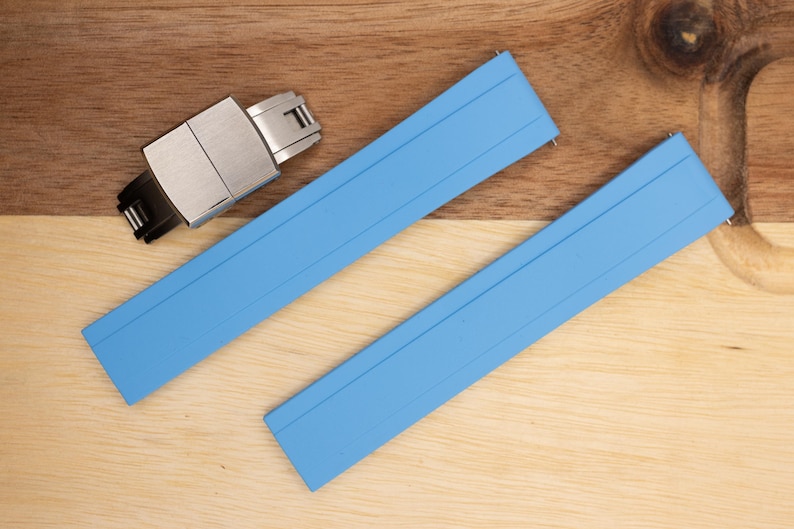 May include: Two light blue watch straps with a silver watch buckle. The straps are made of a rubber-like material and have a smooth, matte finish.