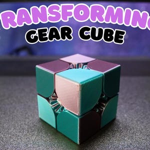 May include: A Transforming Gear Cube in a variety of colors, including teal, pink, and burgundy. The cube is sitting on a dark surface. The text "Transforming Gear Cube" is above the cube in a bubble letter style.