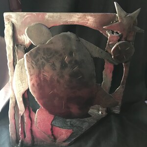 May include: A metal sculpture of a turtle with a star on top. The sculpture is made of welded metal and has a rustic, industrial look. The turtle is in a dark brown color, and the star is in a silver color.
