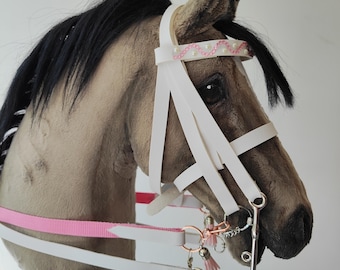 May include: A white leather horse bridle with a pink beaded browband and a silver bit. The bridle is attached to a pink and white reins.