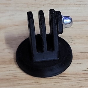 May include: Black plastic GoPro mount with a round base and three prongs. The mount has a silver screw on top.