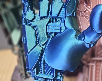 Puede incluir: Una mano robótica de metal azul impresa en 3D con una base hexagonal. La mano está en posición con todos los dedos extendidos.