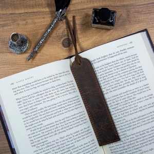 May include: A close-up of a brown leather bookmark with a frayed edge. The bookmark is lying open on a book with text about a hotel and a business meeting. The text on the book reads "Quentins" and "Maeve Binchy".