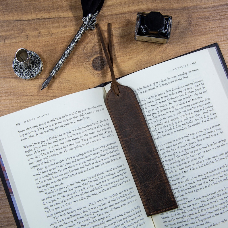 May include: A close-up of a brown leather bookmark with a frayed edge. The bookmark is lying open on a book with text about a hotel and a business meeting. The text on the book reads "Quentins" and "Maeve Binchy".