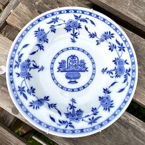 May include: A white ceramic soup bowl with a blue and white floral design. The bowl features a central motif of a basket of flowers with a blue and white design.