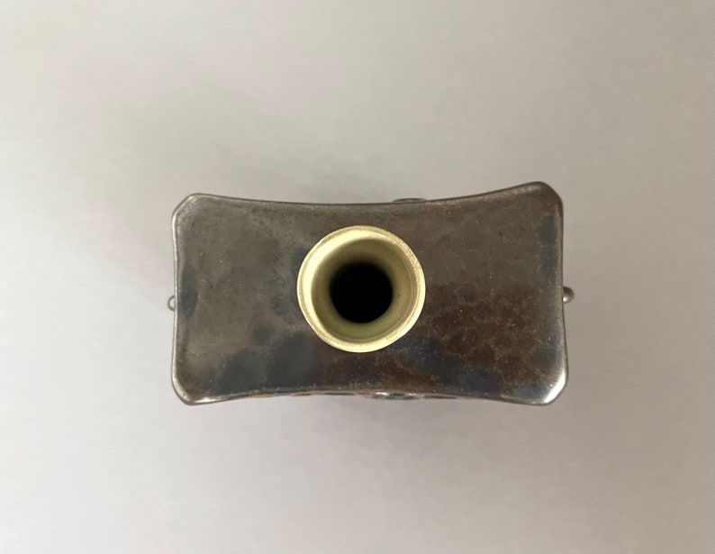 Op de afbeelding: Bovenaanzicht van een zilveren metalen vaas met een ronde opening. De vaas heeft een licht gebogen rechthoekige vorm en een getextureerd oppervlak.