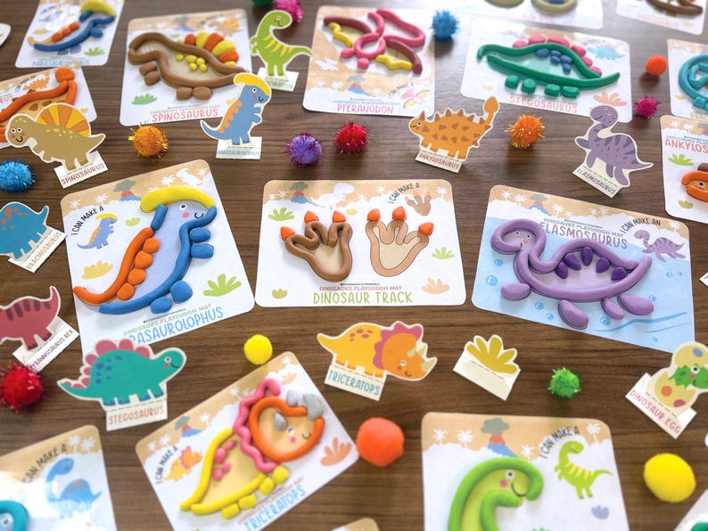 K&ouml;nnte beinhalten: Eine Sammlung von Dinosaurier-Knetkarten mit bunten Tonfiguren verschiedener pr&auml;historischer Kreaturen wie Parasaurolophus, Elasmosaurus und Triceratops sowie Abdr&uuml;cken von Dinosaurierspuren auf wei&szlig;en Karten.