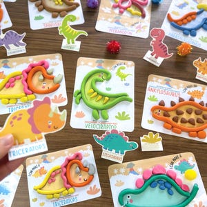 K&ouml;nnte beinhalten: Eine Sammlung von Knete-Aktivit&auml;tskarten zum Thema Dinosaurier mit bunten Knetfiguren von Triceratops, Velociraptor und Ankylosaurus. Jede Karte zeigt eine Cartoon-Dinosaurier-Illustration mit dem entsprechenden Namen darunter.