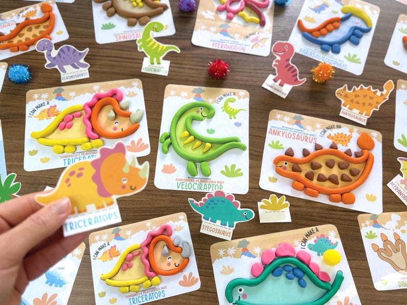 K&ouml;nnte beinhalten: Eine Sammlung von Knete-Aktivit&auml;tskarten zum Thema Dinosaurier mit bunten Knetfiguren von Triceratops, Velociraptor und Ankylosaurus. Jede Karte zeigt eine Cartoon-Dinosaurier-Illustration mit dem entsprechenden Namen darunter.