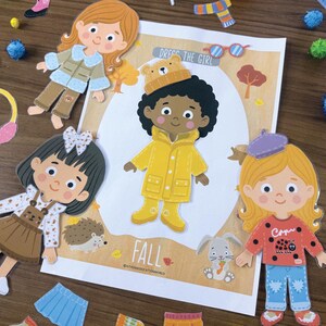 Pode incluir: Um conjunto de bonecas de papel intitulado DRESS THE GIRL FALL com uma personagem central de capa de chuva amarela e gorro de urso, rodeada por tr&ecirc;s bonecas adicionais e v&aacute;rias pe&ccedil;as de vestu&aacute;rio sazonais como camisolas, saias e botas.