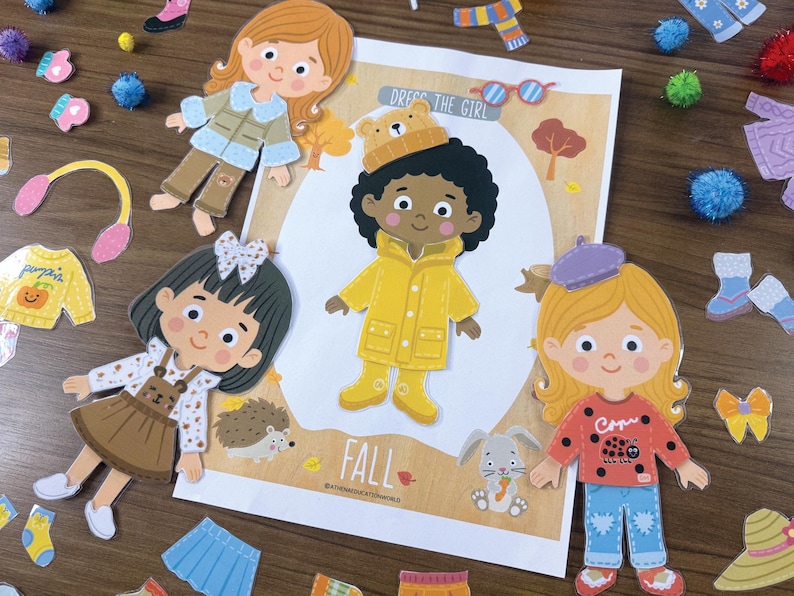 Pode incluir: Um conjunto de bonecas de papel intitulado DRESS THE GIRL FALL com uma personagem central de capa de chuva amarela e gorro de urso, rodeada por tr&ecirc;s bonecas adicionais e v&aacute;rias pe&ccedil;as de vestu&aacute;rio sazonais como camisolas, saias e botas.