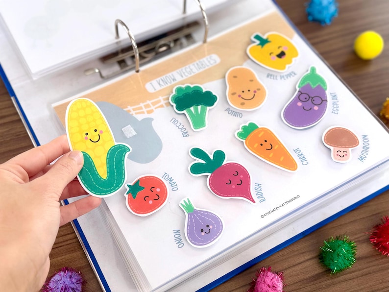 Op de afbeelding: Een educatieve map-pagina getiteld I KNOW VEGETABLES met kleurrijke, cartoonachtige groentestickers met lachende gezichten, waaronder ma&iuml;s, broccoli, aardappel, paprika, aubergine, tomaat, radijs, wortel, champignon en ui met bijbehorende labels.