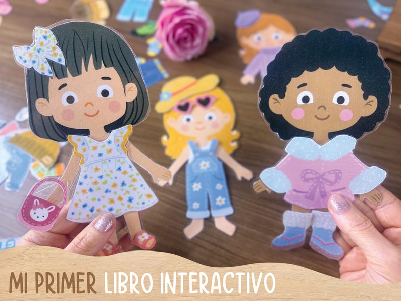 May include: Interactive paper dolls with outfits. The dolls have dark hair, blonde hair, and curly black hair. The dolls are wearing a dress, overalls, and a winter coat. The text "MI PRIMER LIBRO INTERACTIVO" is at the bottom.