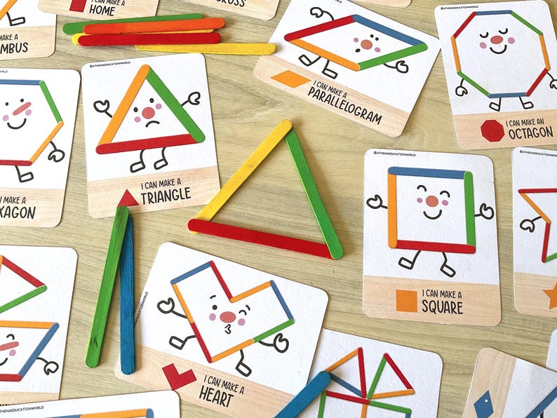 May include: A set of educational cards featuring colorful illustrations of geometric shapes with faces, limbs, and text labels like I CAN MAKE A TRIANGLE, SQUARE, and OCTAGON, accompanied by loose, multi-colored wooden craft sticks for building.