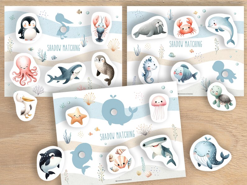 Puede incluir: Tres juegos de emparejamiento de sombras con ilustraciones de acuarela de animales marinos. Cada juego tiene un fondo con una escena de playa y las palabras "SHADOW MATCHING". Las criaturas marinas incluyen un ping&uuml;ino, un pulpo, un tibur&oacute;n, un delf&iacute;n y una ballena.
