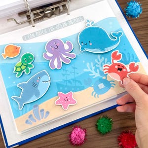 Op de afbeelding: Een educatieve activiteitenpagina getiteld I CAN MATCH THE OCEAN ANIMALS met cartoon-uitsparingen van een walvis, octopus, schildpad, krab, zeester en vis op een blauwe achtergrond met een zandbodem, koraal en een gezonken schip.