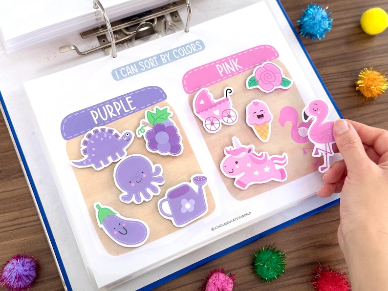 Op de afbeelding: Een educatieve activiteitenpagina getiteld I CAN SORT BY COLORS met twee secties gelabeld PURPLE en PINK. De paarse sectie bevat een dinosaurus, druiven, een octopus en een gieter. De roze sectie bevat een roos, kinderwagen, ijsje, een eenhoorn en een flamingo.