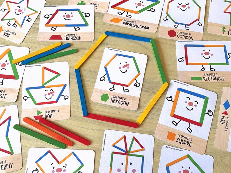 May include: A collection of educational cards featuring colorful illustrations of shapes and objects constructed from craft sticks. A large hexagon is formed in the center using six colored craft sticks, surrounded by cards labeled with names like Trapezoid, Octagon, Rectangle, Square, Boat, and Fish.