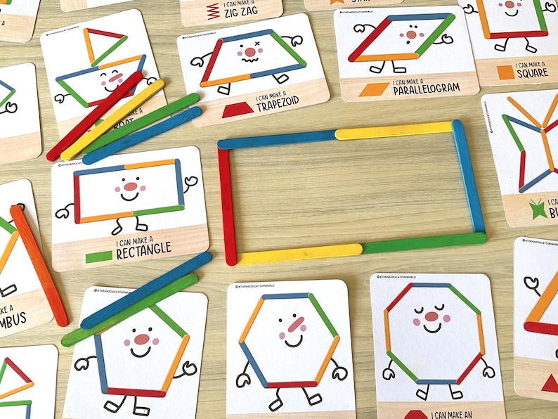 May include: A set of educational cards featuring cartoon shapes with faces, accompanied by colorful wooden craft sticks. The cards display text such as I CAN MAKE A RECTANGLE, I CAN MAKE A TRAPEZOID, and I CAN MAKE A PARALLELOGRAM, with sticks arranged to form a rectangle.