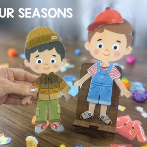 Pode incluir: Duas bonecas de papel planas e ilustradas com o texto FOUR SEASONS. Uma boneca usa um gorro castanho, um casaco castanho e cal&ccedil;as verdes. A outra usa um bon&eacute; vermelho, uma camisola &agrave;s riscas vermelhas e brancas e jardineiras azuis com sand&aacute;lias.