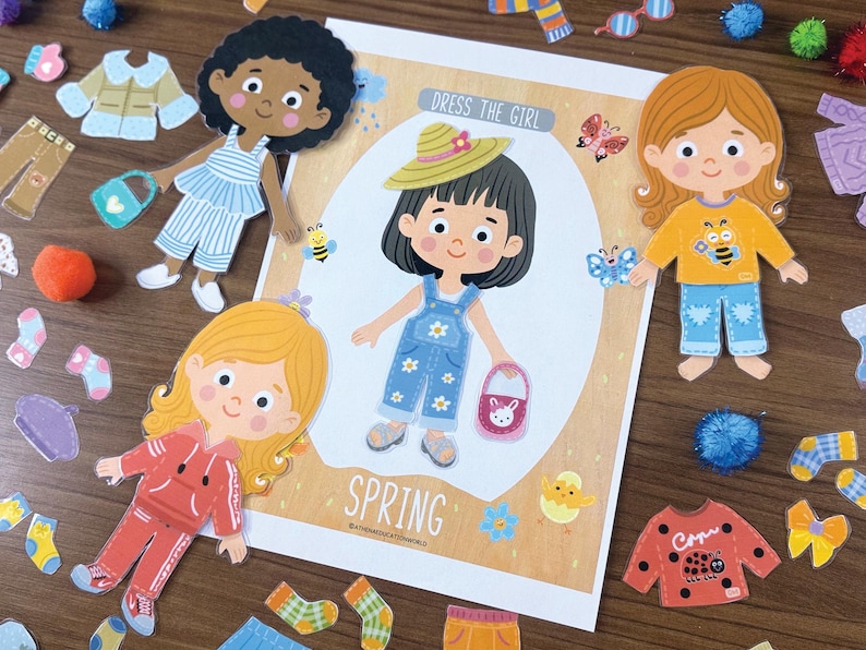 Pode incluir: Um conjunto de bonecas de papel intitulado Dress The Girl Spring com uma personagem central vestindo jardineiras jeans azuis com flores brancas, um chap&eacute;u de palha e uma bolsa rosa, rodeada por bonecas adicionais e v&aacute;rias pe&ccedil;as de roupa.