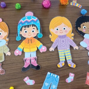 Pode incluir: Quatro bonecas de papel com diversas cores de cabelo e tons de pele, cada uma vestindo roupas de inverno, incluindo gorros, casacos, su&eacute;teres e botas. O conjunto inclui pe&ccedil;as de roupa de papel adicionais, como cal&ccedil;as e meias espalhadas.