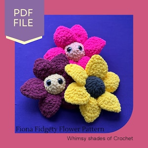 May include: Three crocheted flower toys with googly eyes. The flowers are pink, purple, and yellow. The flowers are arranged in a pile on a blue background. The text "Fiona Fidgety Flower Pattern" and "Whimsy shades of Crochet" are at the bottom of the image.