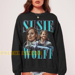 May include: Black sweatshirt with a blue graphic print of Susie Wolff, a woman in a racing suit, and a vintage Mercedes-Benz car. The text "Susie Wolff" is printed in blue.