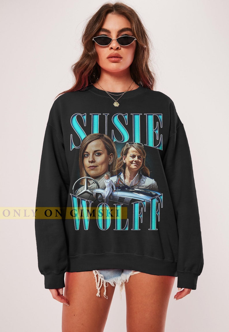 May include: Black sweatshirt with a blue graphic print of Susie Wolff, a woman in a racing suit, and a vintage Mercedes-Benz car. The text "Susie Wolff" is printed in blue.