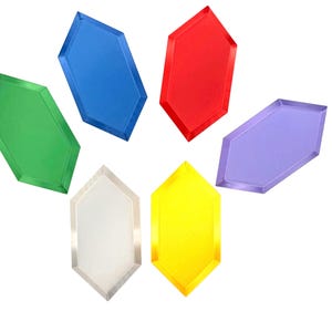 May include: A collection of six translucent, hexagonal-shaped gems in vibrant colors including green, blue, red, purple, yellow, and a clear white. Each gem features beveled edges and a smooth, flat surface, arranged in a scattered pattern.