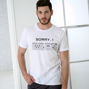May include: White t-shirt with the text "SORRY, I" and a series of guitar chord diagrams.
