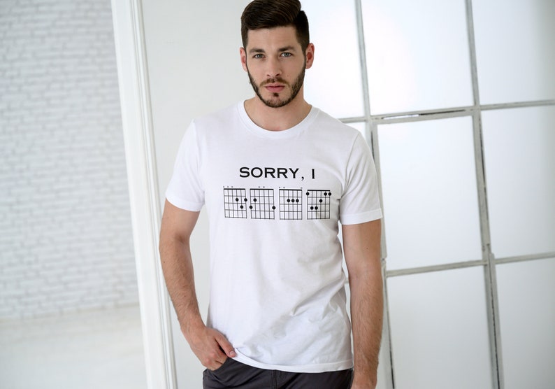 May include: White t-shirt with the text "SORRY, I" and a series of guitar chord diagrams.