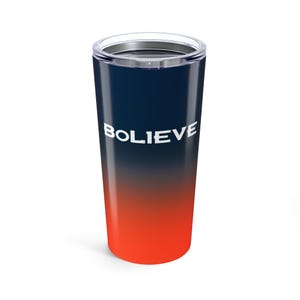May include: A stainless steel tumbler with a colour gradient. The top is navy blue, fading to a deep orange at the bottom. The word "BOLIEVE" is printed in white, centered on the tumbler. The tumbler has a clear lid.