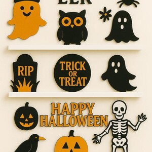 May include: Halloween-themed decorations on white shelves. Includes orange and black cutouts of a ghost, owl, bats, spider, tombstone, and pumpkins. Text includes "EEK" and "HAPPY HALLOWEEN".