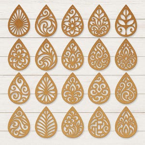 May include: A collection of twenty teardrop-shaped wooden earrings with intricate cut-out designs. The earrings feature various patterns, including floral, geometric, and abstract motifs. The earrings are displayed on a white wooden surface.