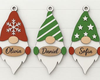 May include: Three wooden Christmas gnome ornaments. Each gnome has a different colored hat: red with a snowflake, green with white stripes, and green with white stars. Each ornament has a name: Olivia, Daniel, and Sofia.