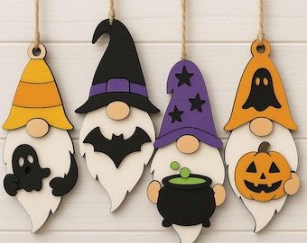 Może przedstawiać: Cztery drewniane ozdoby z gnomami na Halloween zawieszone na sznurku. Każdy gnom ma białą brodę, okrągły nos i inny kapelusz: pomarańczowo-żółty, czarny z nietoperzem, fioletowy z gwiazdami i pomarańczowy z duchem i dynią.