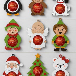 Puede incluir: Adornos navideños de madera con formas de pingüino, reno, perro, elfo, ángel, niño, Papá Noel, árbol de Navidad y oso. Cada adorno contiene un chocolate Lindor rojo y detalles festivos.