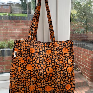 Può includere: Borsa tote arancione e nera con un motivo batik. La borsa ha due lunghe cinghie e la parola "batik" è stampata sul lato.