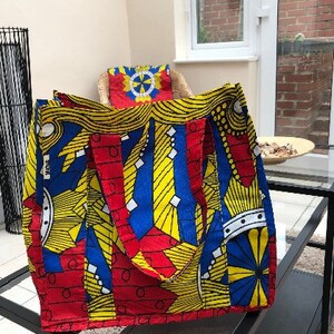 May include: A large tote bag with a colourful African print design. The bag is made of fabric and has two handles. The print features yellow, red, blue, and white geometric shapes.