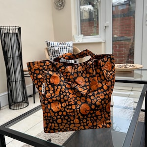 Può includere: Una borsa tote nera e arancione con un motivo circolare. La borsa ha un'etichetta nera con la parola "SOKO" stampata su di essa.