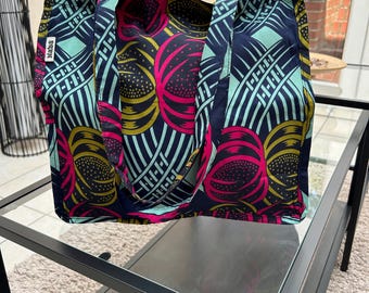 Pode incluir: Uma grande sacola com um padrão abstrato colorido. A sacola apresenta um fundo azul marinho com desenhos circulares rosa, amarelo e verde-azulado. A sacola tem formato retangular com alças e a palavra "Nabs" na lateral.