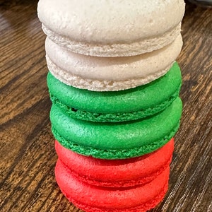 May include: A stack of four macarons, with the top two being white, the next green, and the bottom red.