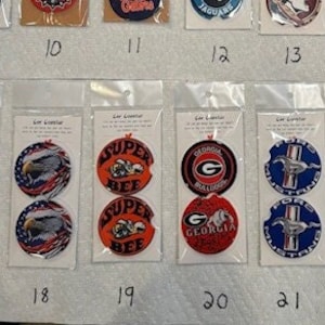 May include: A collection of 24 round, double-sided coasters with various designs. The coasters are packaged individually in clear plastic bags. The designs include logos, animals, and abstract patterns.