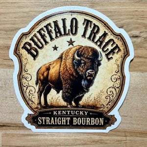 May include: A die-cut sticker featuring a brown bison illustration centered within a decorative frame. The text reads BUFFALO TRACE at the top and KENTUCKY STRAIGHT BOURBON at the bottom, with two small stars positioned above the bison's back.