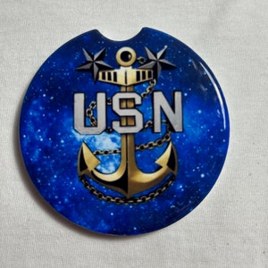 May include: A blue and gold car coaster with a galaxy background. The coaster features a gold anchor with a chain, two stars, and the letters "USN".