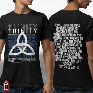 Könnte beinhalten: Schwarzes T-Shirt mit einer weißen Grafik eines Trinitätssymbols und dem Text "TRINITY" und "THREE IN ONE", der viermal wiederholt wird. Die Rückseite des Shirts hat weißen Text, der lautet "JESUS, WHEN HE WAS BAPTIZED, WENT UP DIRECTLY FROM THE WATER: AND BEHOLD, THE HEAVENS WERE OPENED TO HIM. HE SAW THE SPIRIT OF GOD DESCENDING AS A DOVE, AND COMING ON HIM, BEHOLD, A VOICE OUT OF THE HEAVENS SAID, THIS IS MY BELOVED SON, WITH WHOM I AM WELL PLEASED." -MATTHEW 3:16-17